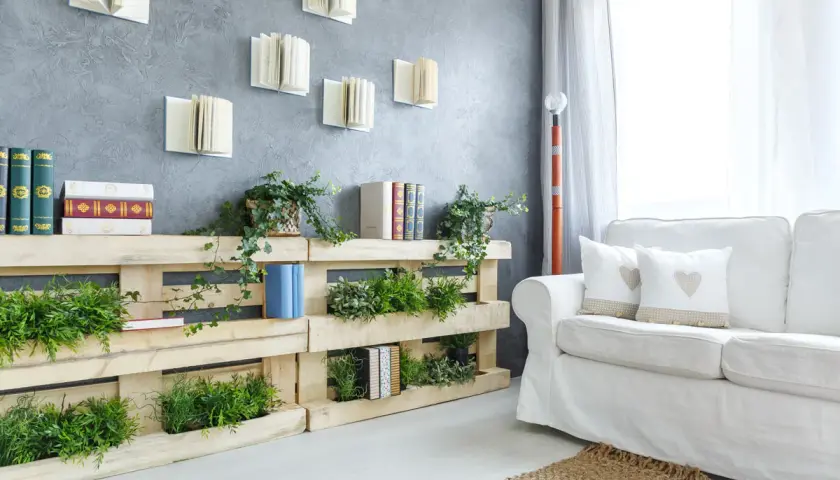 Pareti con bancali che ospitano piante verdi e libri, creando un angolo lettura naturale e accogliente.