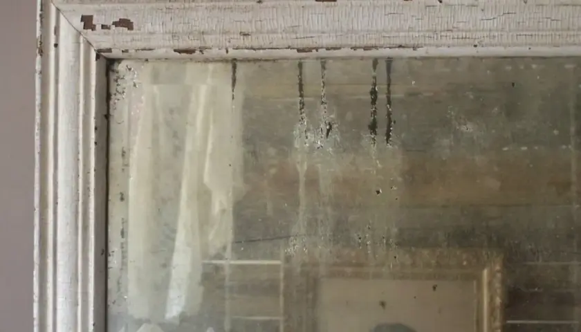 Cornice scrostata e specchio antico, con riflessi di un ritratto e tendaggi. Un modo per come invecchiare uno specchio, con patina del tempo.