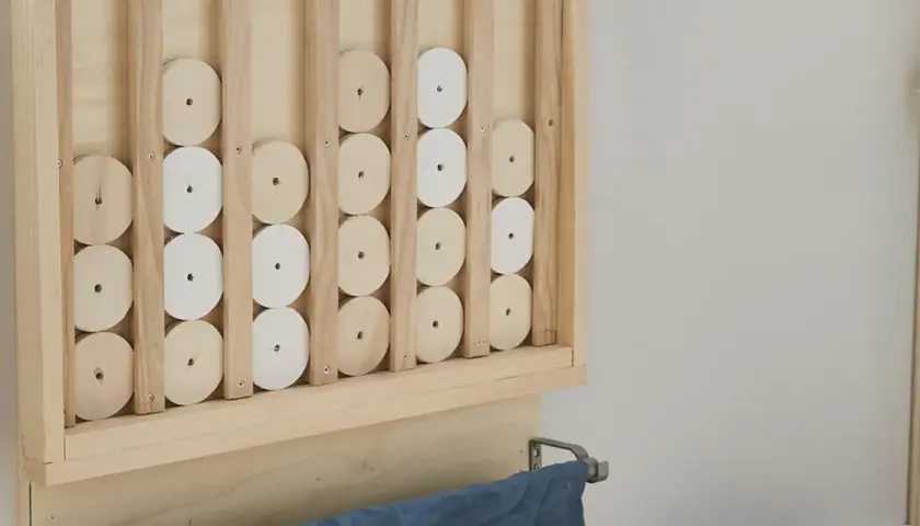 Un gioco da tavolo fai da te in legno, con dischi bianchi e naturali che scorrono su binari verticali.