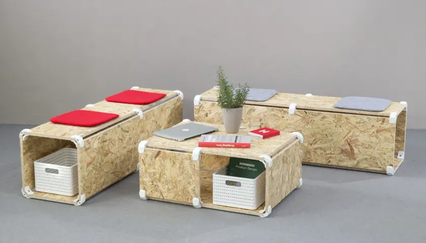 Set di mobili in OSB fai da te: tavolino e panche modulari con cuscini rossi e grigi, cestini portaoggetti e libri.