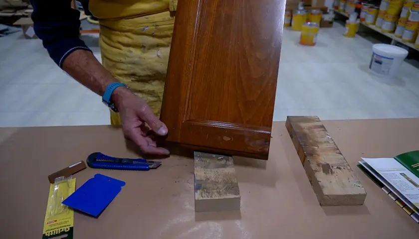 Un falegname esamina un pannello di legno con un piccolo buco, pronto per la riparazione.