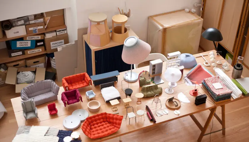 Modelli di mobili in miniatura, tessuti e materiali da artigianato disposti su un tavolo di legno. Un'ispirazione per creare, inga sempé.