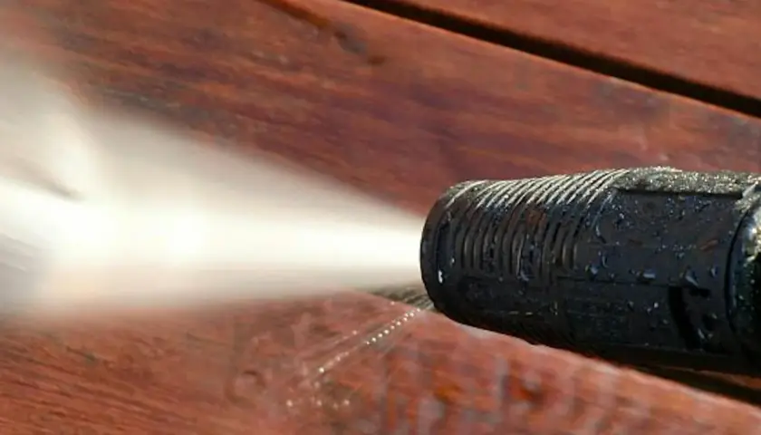 Ugello idropulitrice spruzza acqua su un deck in legno per eliminare odore vernice legno.