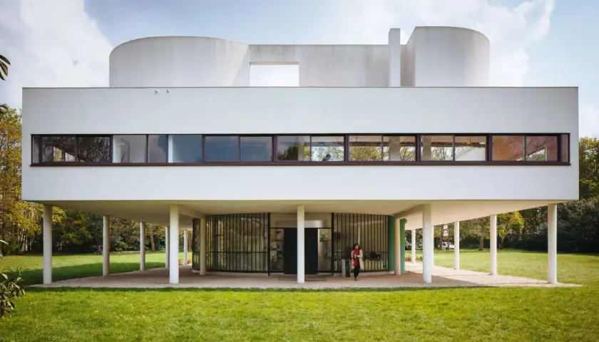 Villa Savoye, capolavoro di Le Corbusier, si erge su pilastri bianchi, con finestre a nastro e forme curve che sfidano la gravità.