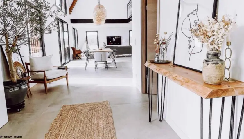 Una consolle fai da te con piano in legno grezzo e gambe sottili, decorata con un vaso di fiori secchi e un quadro astratto.