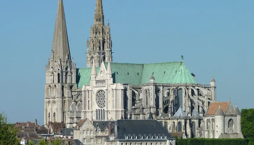 Imponente cattedrale gotica con guglie svettanti e tetto verde, che domina un paesaggio urbano sotto un cielo azzurro.