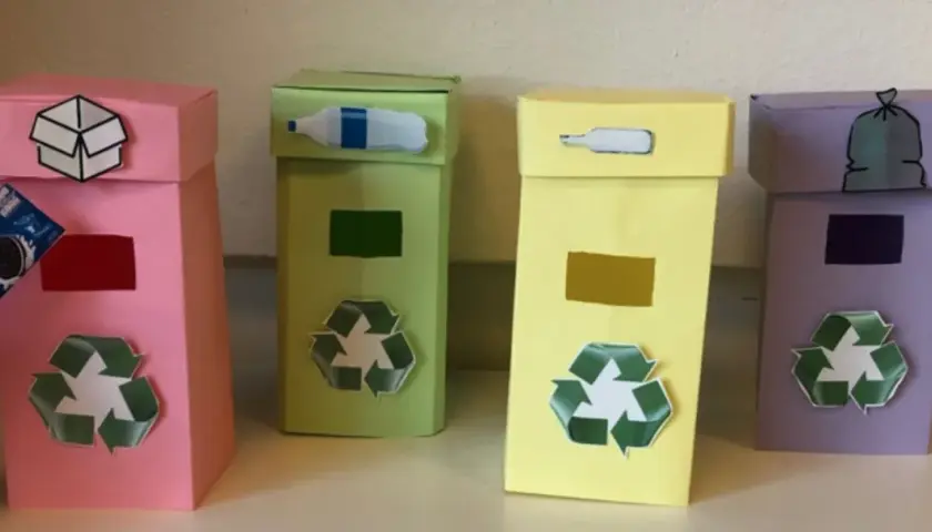 Quattro colorati contenitori per la raccolta differenziata fai da te, con simboli e immagini che indicano cosa gettare.