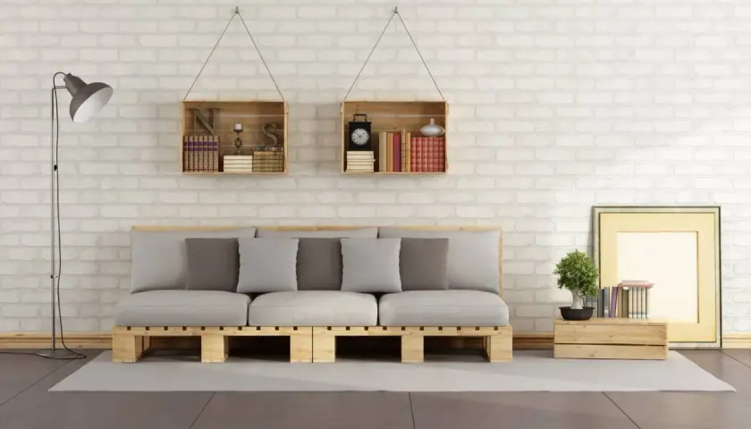 Divano pallet fai da te con cuscini grigi e bianchi, librerie a muro in legno e lampada da terra.