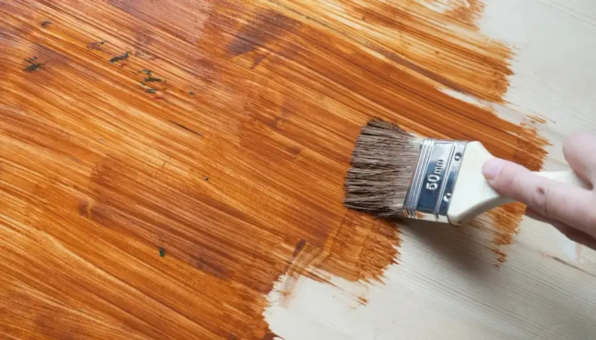 Pennello applica vernice marrone su legno, rinnovando una superficie già verniciata.