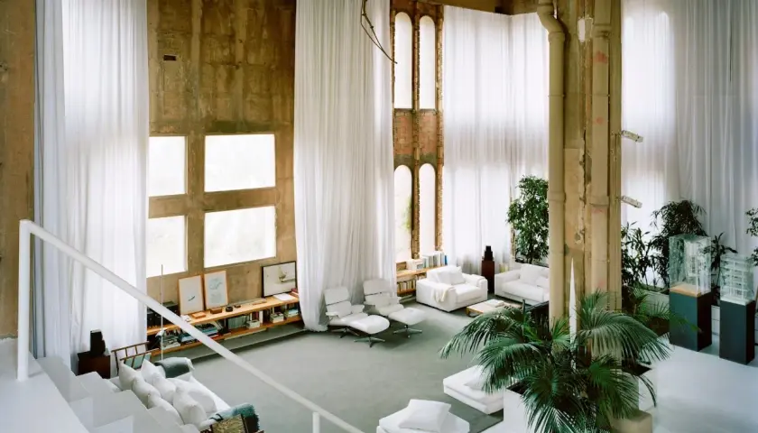 Interno spazioso con tende bianche, finestre quadrate e un'architettura industriale che ricorda lo stile di Ricardo Bofill.