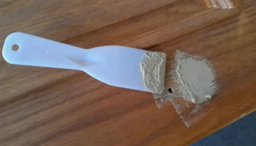 Spatola con stucco per legno fai da te, pronta per riparare un piccolo foro su una superficie di legno.