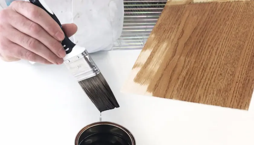 Pennello intinto in una latta, pronto per applicare un prodotto che mostra la differenza tra flatting e impregnante su legno.