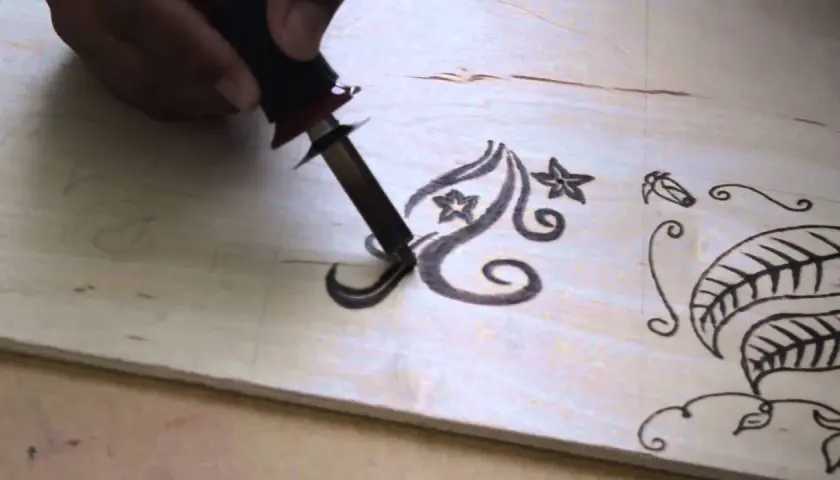 Mano che usa un pirografo per disegnare motivi floreali su legno. Impara come disegnare sul legno con questa tecnica.