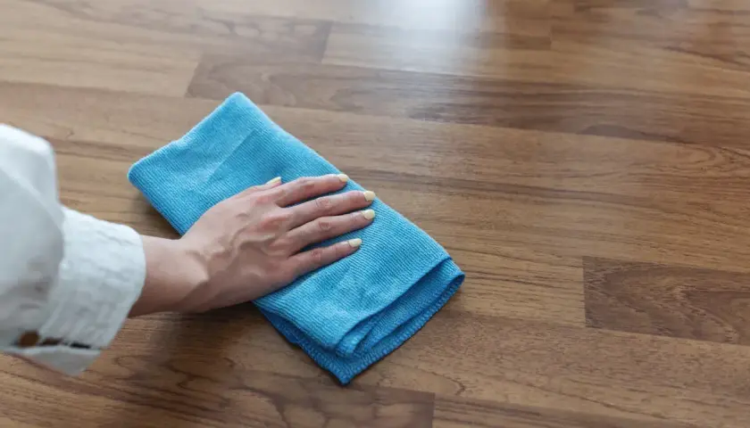 Mano con panno blu che pulisce il pavimento in legno, un metodo efficace per come togliere la colla dal legno.