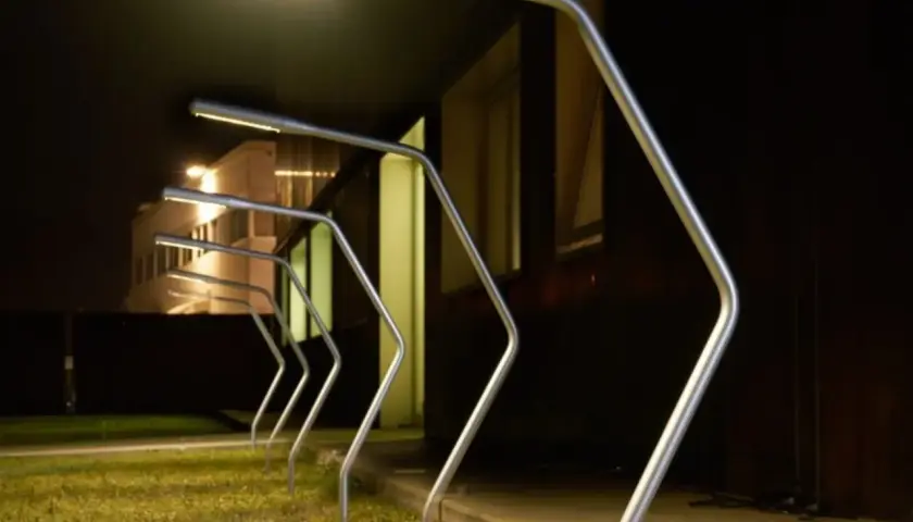 Row of modern silver garden lamps with bright LED lights at night.