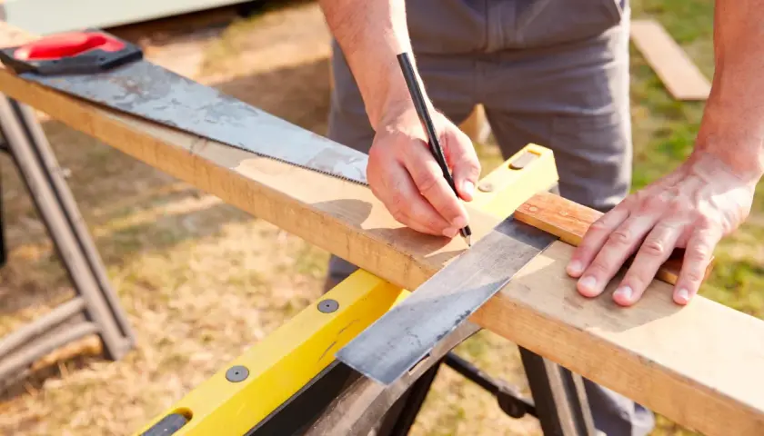 Mani che prendono le **misure per fare una squadra** perfetta su un pezzo di legno, con una sega e una matita a portata di mano.