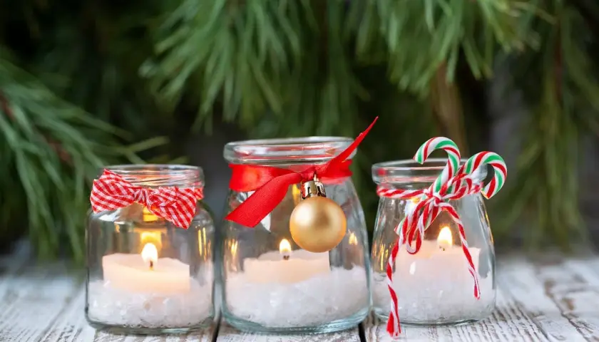 Candele in barattoli decorati con nastri rossi, fiocchi e palline dorate. Un'idea per addobbi natalizi fai da te, con un tocco di magia.