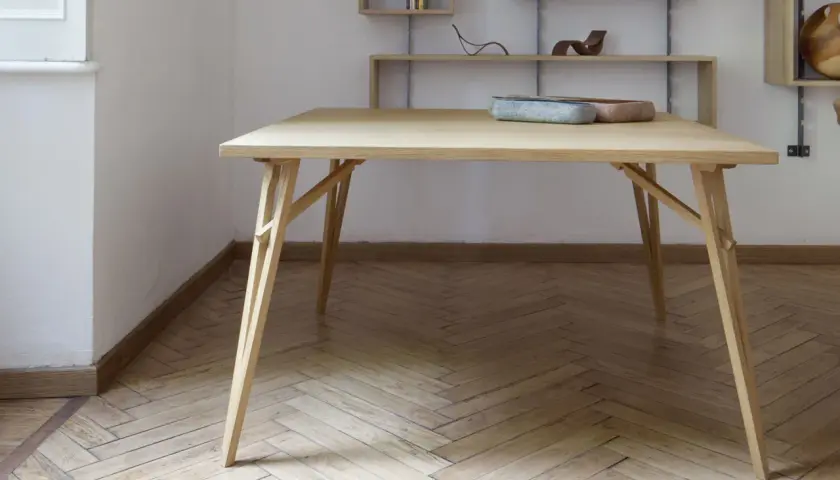 Tavolo pieghevole fai da te in legno chiaro, con gambe a incastro e piano squadrato. Due ciotole decorative sul piano.