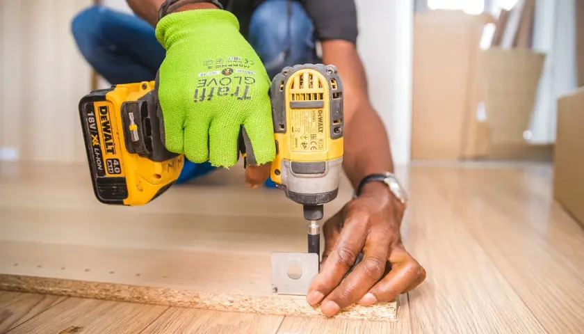 Uomo con guanti verdi usa un trapano per fresare il legno, creando fori precisi per un progetto fai-da-te.