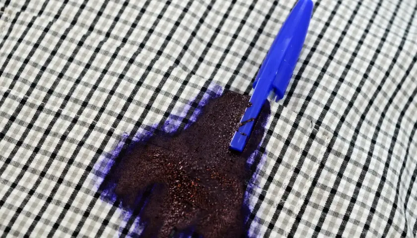 Una penna blu ha creato una grossa macchia d'inchiostro su una camicia a quadri.