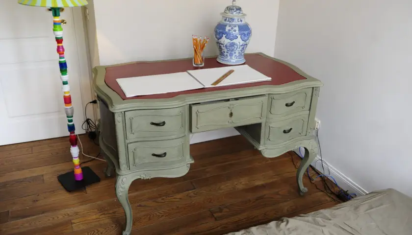 Scrivania in stile shabby chic, con finitura chalk paint fai da te. Penzoli, un righello e un vaso decorato completano la scena.