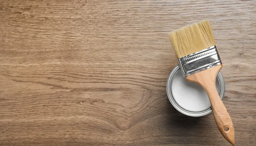Pennello pronto per dipingere legno. La latta di vernice bianca è aperta, il legno è pronto per il restauro.