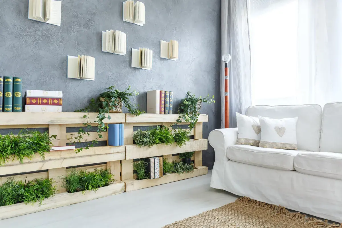 Pareti con bancali che ospitano piante verdi e libri, creando un angolo lettura naturale e accogliente.