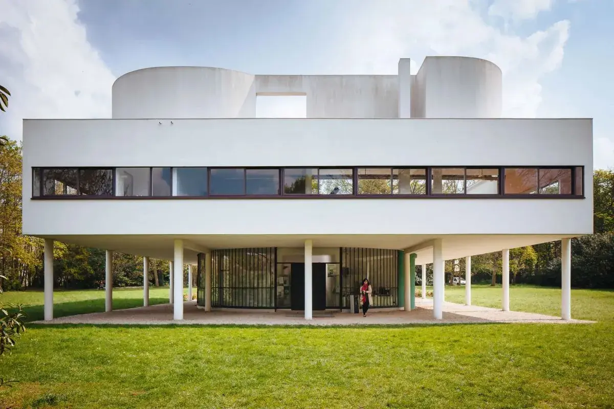 Villa Savoye, capolavoro di Le Corbusier, si erge su pilastri bianchi, con finestre a nastro e forme curve che sfidano la gravità.