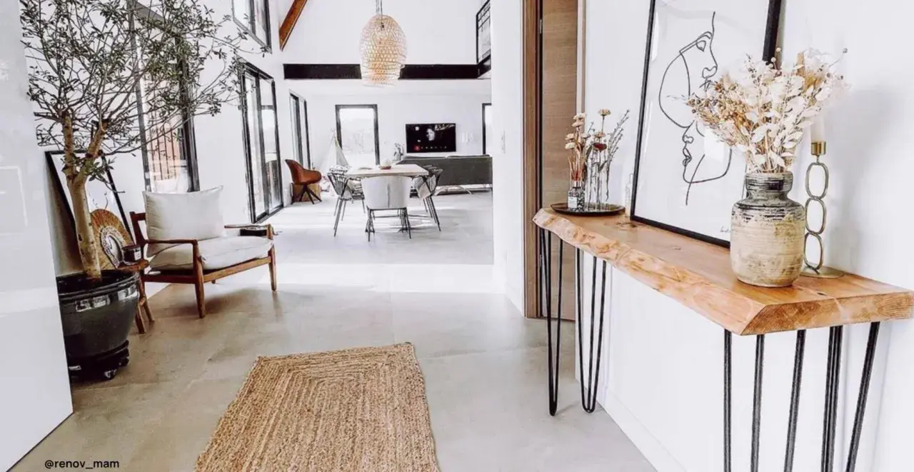 Una consolle fai da te con piano in legno grezzo e gambe sottili, decorata con un vaso di fiori secchi e un quadro astratto.