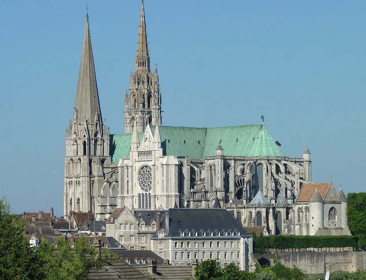 Imponente cattedrale gotica con guglie svettanti e tetto verde, che domina un paesaggio urbano sotto un cielo azzurro.