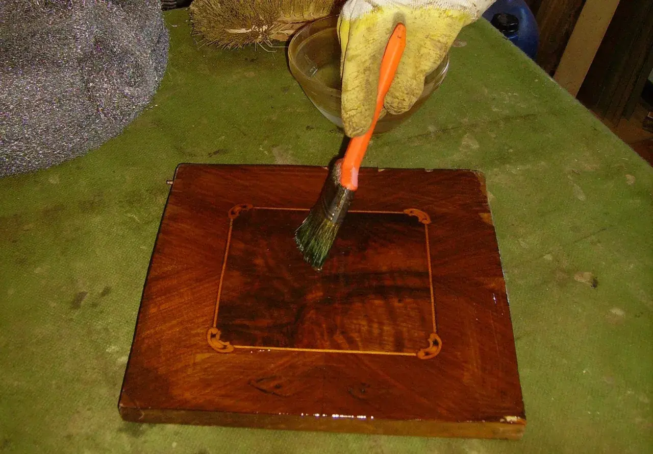 Guanto giallo applica liquido con pennello arancione su un mobile in legno scuro, per imparare come sverniciare un mobile.