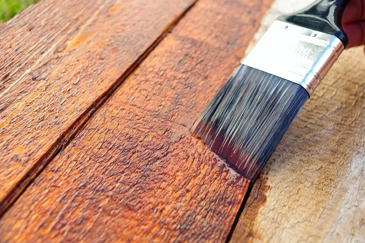 Pennello stende impregnante su assi di legno grezzo, creando una finitura protettiva e colorata.