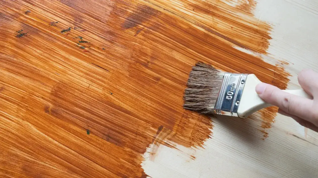 Pennello applica vernice marrone su legno, rinnovando una superficie già verniciata.