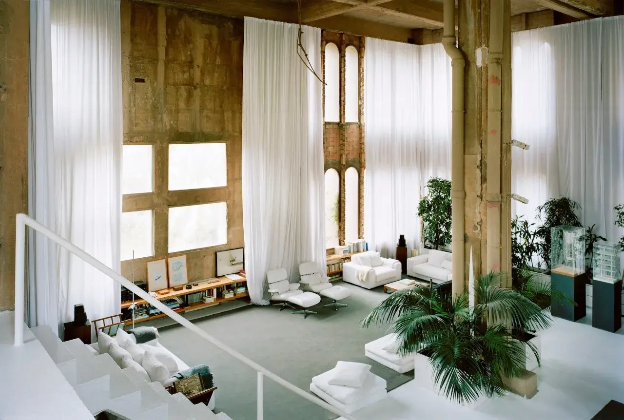 Interno spazioso con tende bianche, finestre quadrate e un'architettura industriale che ricorda lo stile di Ricardo Bofill.