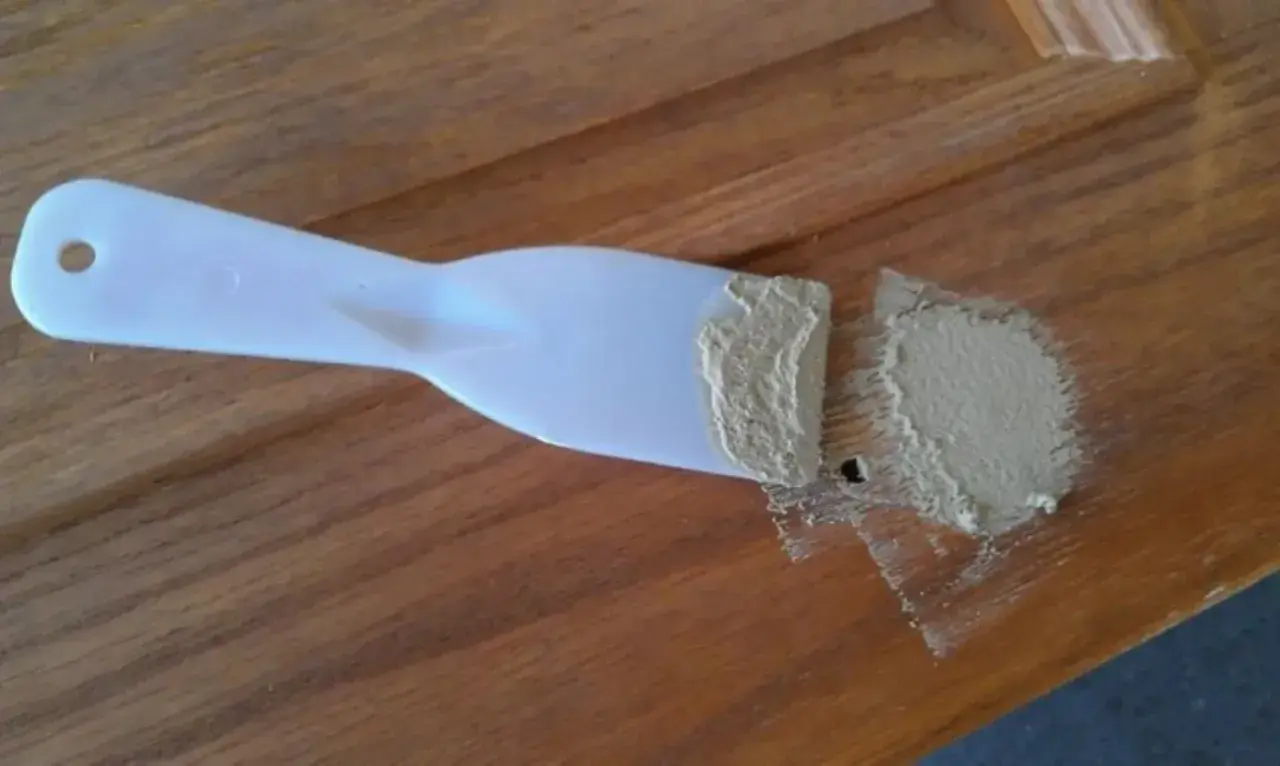 Spatola con stucco per legno fai da te, pronta per riparare un piccolo foro su una superficie di legno.