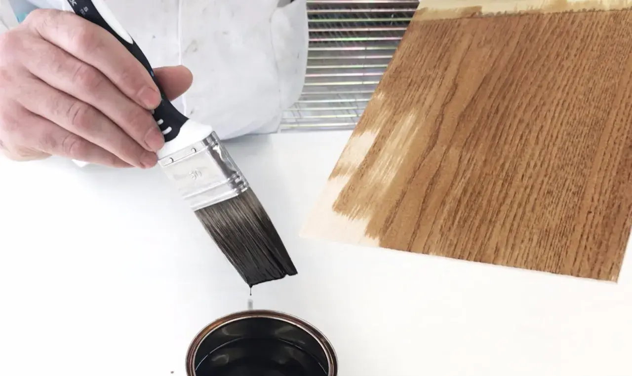 Pennello intinto in una latta, pronto per applicare un prodotto che mostra la differenza tra flatting e impregnante su legno.