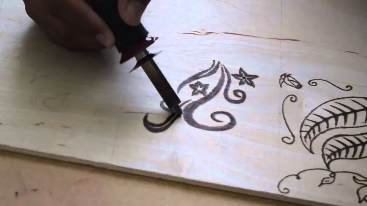Mano che usa un pirografo per disegnare motivi floreali su legno. Impara come disegnare sul legno con questa tecnica.