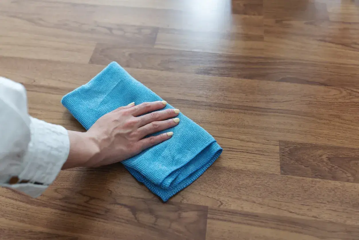 Mano con panno blu che pulisce il pavimento in legno, un metodo efficace per come togliere la colla dal legno.