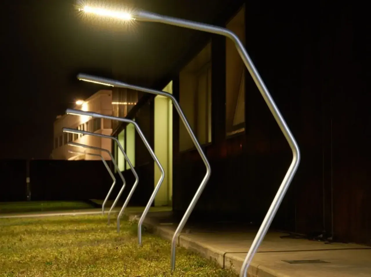 Row of modern silver garden lamps with bright LED lights at night.