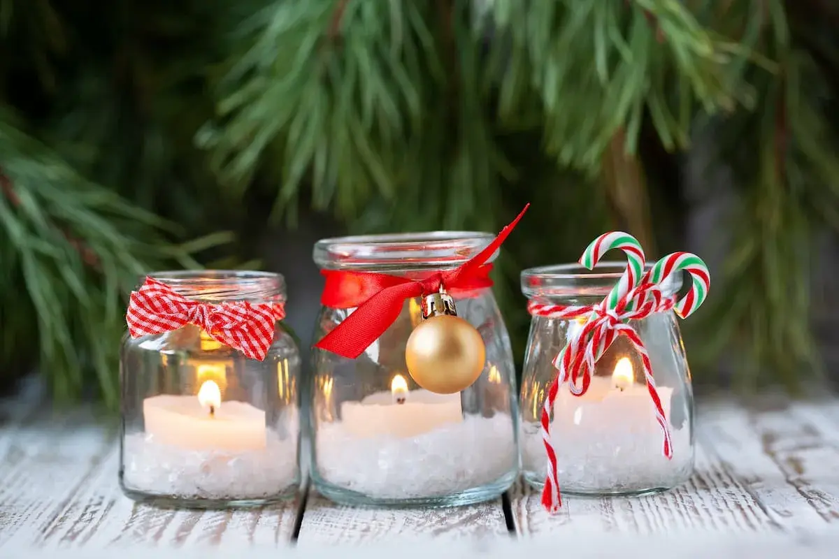 Candele in barattoli decorati con nastri rossi, fiocchi e palline dorate. Un'idea per addobbi natalizi fai da te, con un tocco di magia.