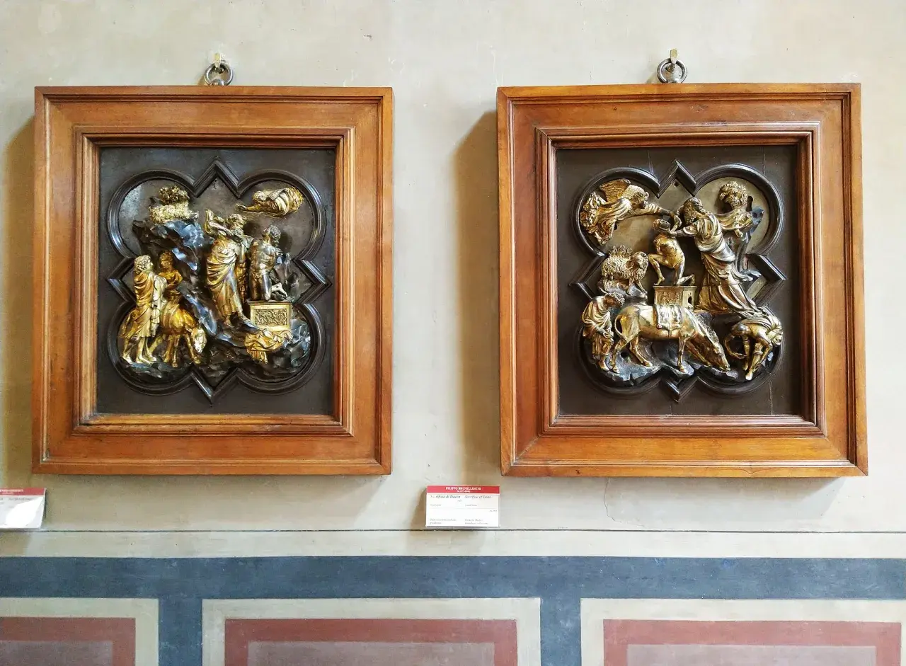 Due bassorilievi dorati incorniciati in legno, opere di Brunelleschi, raffigurano scene bibliche con figure umane e animali.