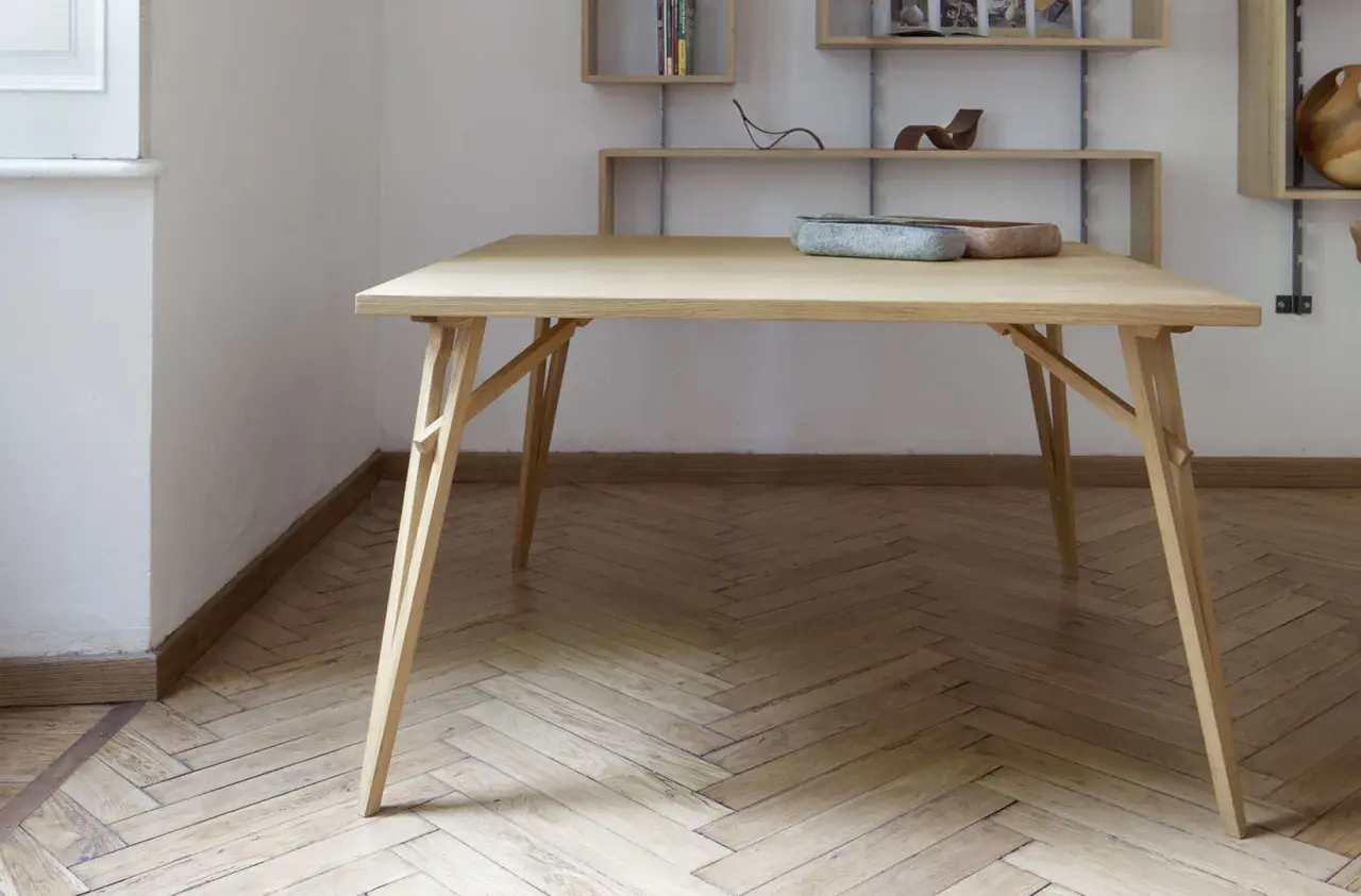 Tavolo pieghevole fai da te in legno chiaro, con gambe a incastro e piano squadrato. Due ciotole decorative sul piano.