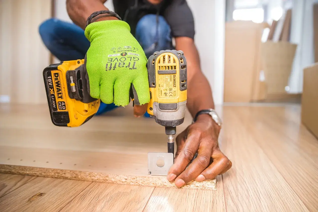 Uomo con guanti verdi usa un trapano per fresare il legno, creando fori precisi per un progetto fai-da-te.