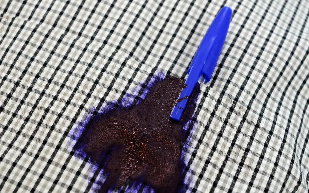 Una penna blu ha creato una grossa macchia d'inchiostro su una camicia a quadri.