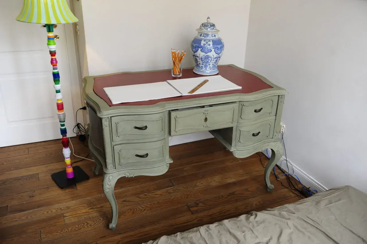 Scrivania in stile shabby chic, con finitura chalk paint fai da te. Penzoli, un righello e un vaso decorato completano la scena.