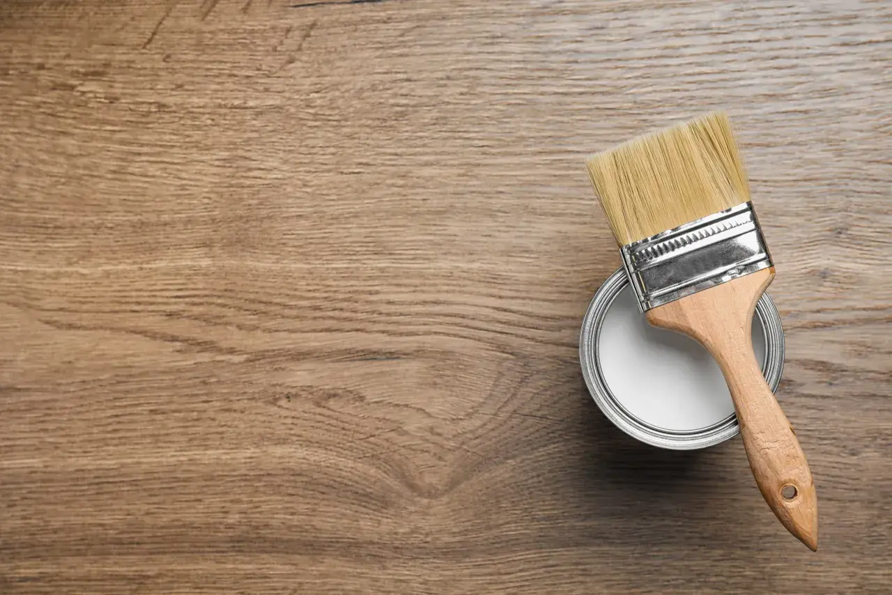 Pennello pronto per dipingere legno. La latta di vernice bianca è aperta, il legno è pronto per il restauro.