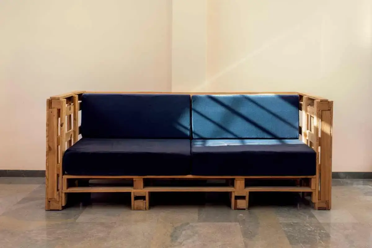 Divano pallet fai da te con cuscini blu scuro e blu acceso, illuminato da raggi di sole obliqui.