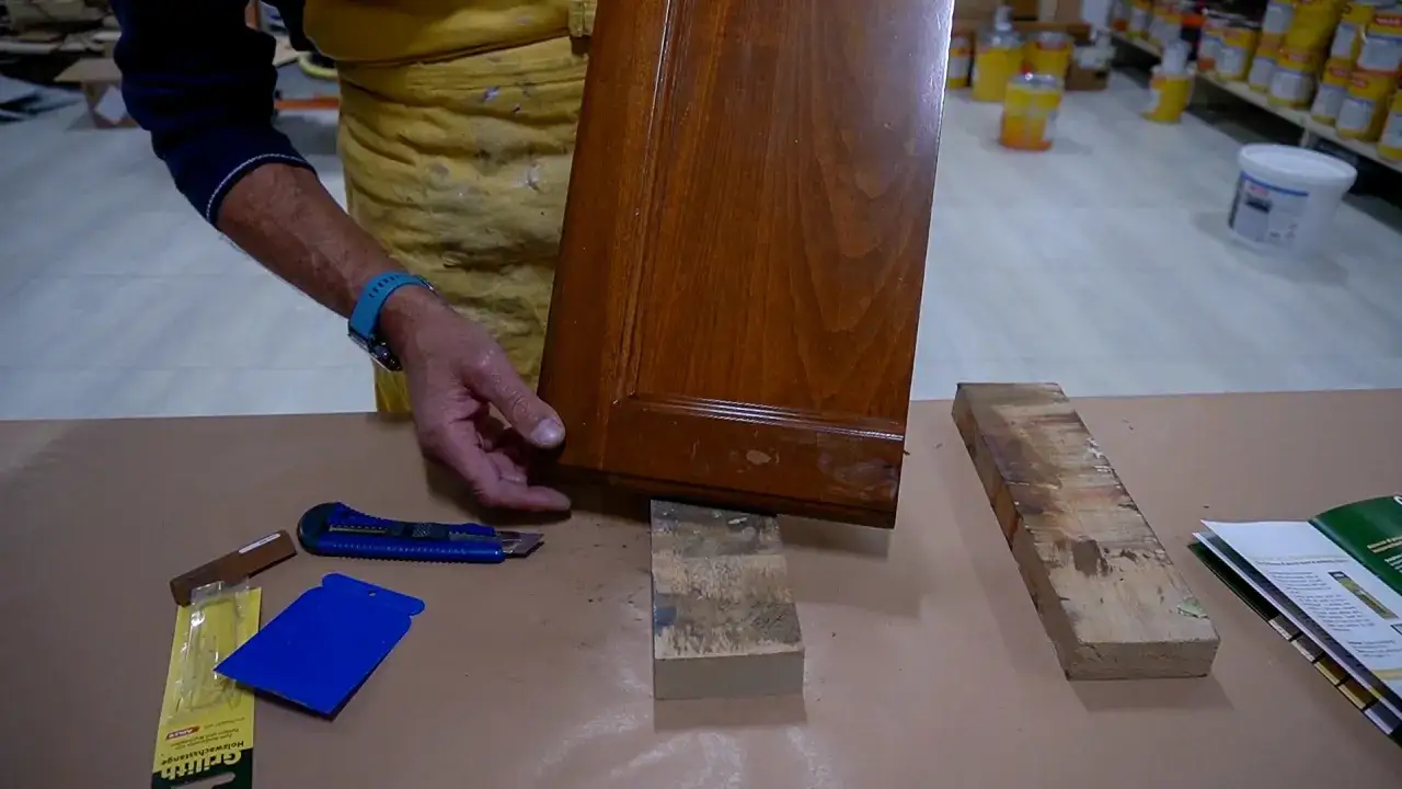 Un falegname esamina un pannello di legno con un piccolo buco, pronto per la riparazione.