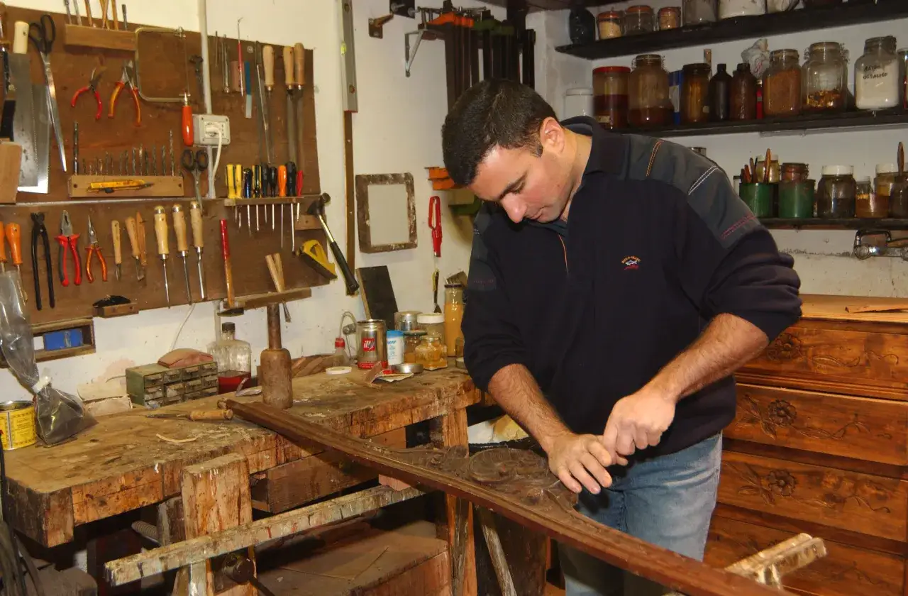 Un restauratore al lavoro nella sua bottega, circondato da attrezzi e materiali.