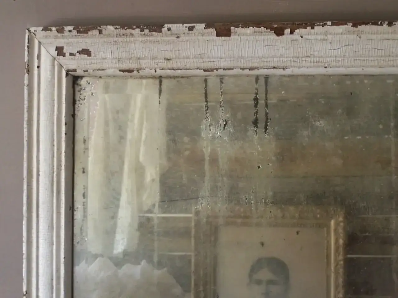 Cornice scrostata e specchio antico, con macchie che raccontano come invecchiare uno specchio. Riflesso di un ritratto e tendaggi.